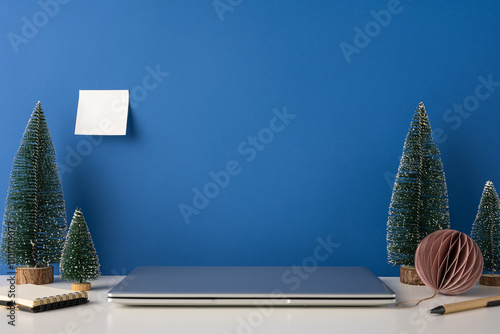 A side view modern workspace featuring Scandinavian decor with a winter theme. Small decorative trees and a neat desk setup create a cozy and minimalistic environment