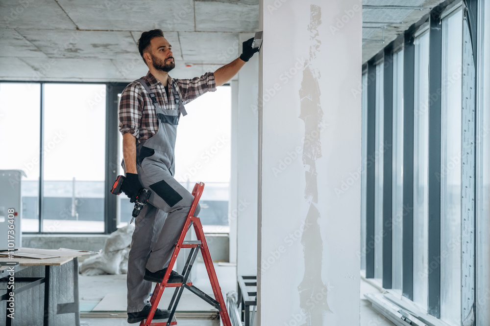 On the ladder. A man is renovating an unfinished room On the ladder. A man is renovating an unfinished room