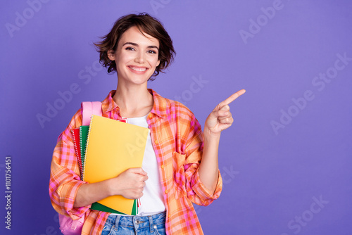 Portrait of pretty young lady point finger empty space ad wear shirt isolated on purple color background