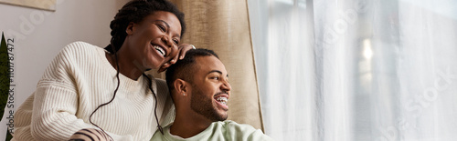 African American couple enjoys quality time together in cozy sweaters, laughing and relaxed at home.