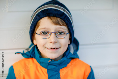 Portrait of little cute school kid boy with glasses and colorful winter fashion clothes. Child smiling and having fun with the camera. Winter, spring or autumn fashion. Kid with missing front teeth