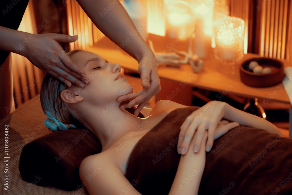 Fototapeta premium Caucasian woman enjoying relaxing anti-stress head massage and pampering facial beauty skin recreation leisure in warm candle lighting ambient salon spa in luxury resort or hotel. Quiescent