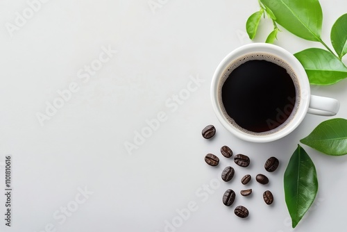 Dark coffee in a bowl accompanied by fresh leaves and coffee beans on a white...
