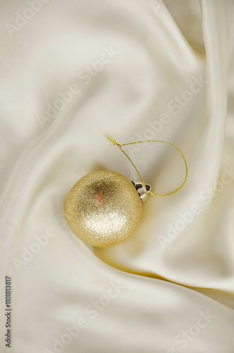 Gold Christmas Ornament on Soft White Fabric. Christmas decoration featuring a glittering golden bauble resting on a smooth white fabric background with soft, warm fairy lights, minimalism and winter-