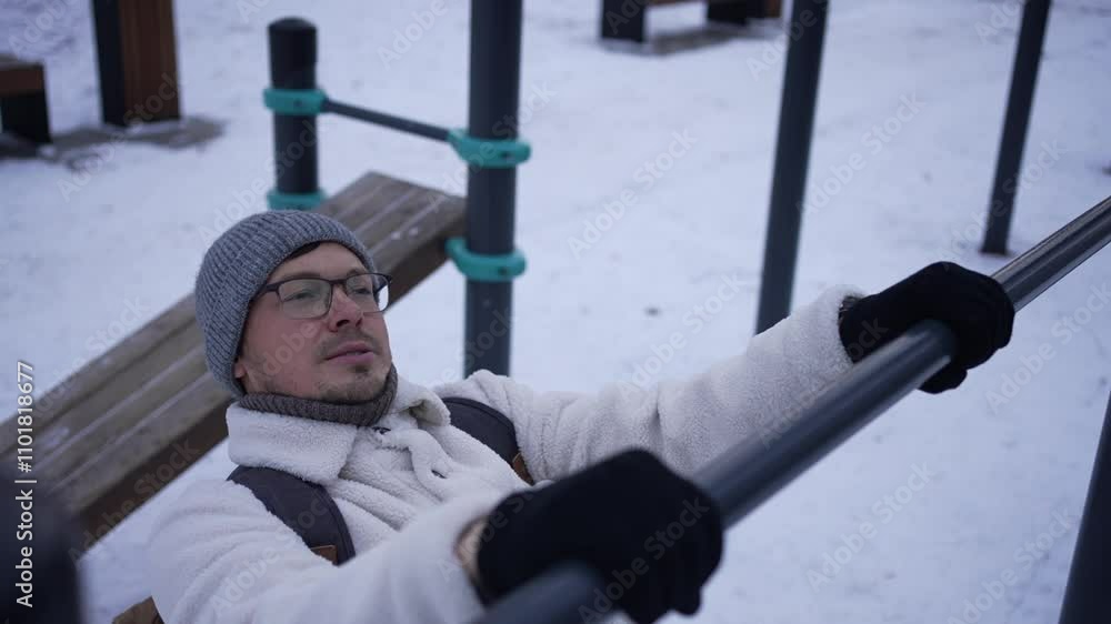 Young man is working out on a cold winter day. He is wearing warm clothes and gloves as he exercises on an outdoor pull up bar Young man is working out on a cold winter day. He is wearing warm clothes and gloves as he exercises on an outdoor pull up bar