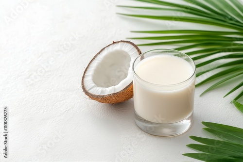 Coconut milk in a clear glass beside a halved coconut on a marble surface wit...