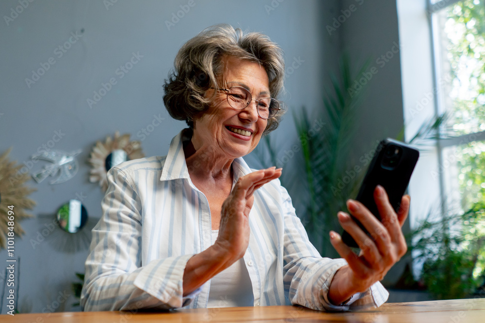 close-up of a very elderly gray-haired grandmother in a light blouse with a slight smile sitting against the background of a blue wall with large indoor plants writing a message on the phone close-up of a very elderly gray-haired grandmother in a light blouse with a slight smile sitting against the background of a blue wall with large indoor plants writing a message on the phone