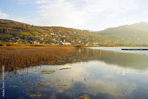 An autumn evening on Lake Plav: water reflecting clouds, thickets of sedge and reeds, houses built on the slope and mountains in the background. Life on the north-eastern border of Montenegro. photo