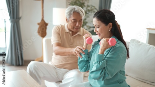 Happy elderly couple exercising together with dumbbells at home, focusing on muscle strength, joint health, and physical wellness for improved mobility and healthy aging. Retirement concept. Myrmidon.