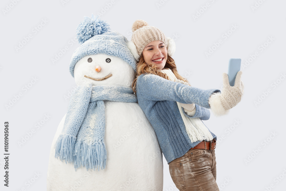 Happy young woman taking a selfie with a snowman, dressed in warm knitted winter clothing. A festive ski trip during the Christmas holidays in the winter season. Social media influencer travel concept Happy young woman taking a selfie with a snowman, dressed in warm knitted winter clothing. A festive ski trip during the Christmas holidays in the winter season. Social media influencer travel concept