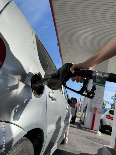 A person is filling up a silver car at a gas station