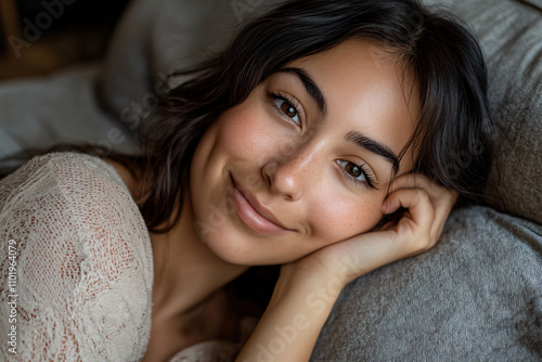 Close-up portrait of a happy, smiling woman relaxing on a couch at home. She is looking at the camera and resting her head on her hand, with her eyes open. Captured with a Sony Alpha A7 III, the image photo