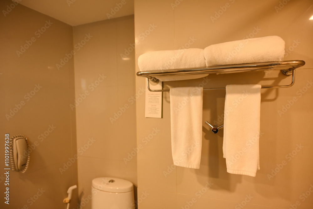 A neatly arranged towel rack with white towels above in a minimalist hotel bathroom, showcasing cleanliness and functionality A neatly arranged towel rack with white towels above in a minimalist hotel bathroom, showcasing cleanliness and functionality