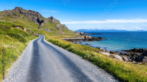 A lonely road hugs the rugged coastline, framed by dramatic mountains and a blue sky, offering a tranquil escape and embodying the essence of solitary exploration.