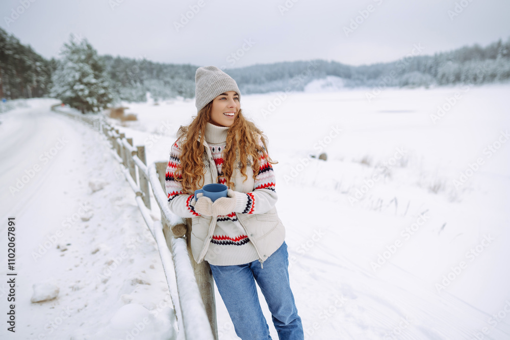 Fototapeta premium Happy woman drinks a hot drink from a thermos in a winter snowy forest. Warm up in frozen winter forest, warm hands. travel, wanderlus.