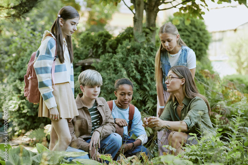 Young female botanist showing rare plants to group of teen students while visiting local botanical garden