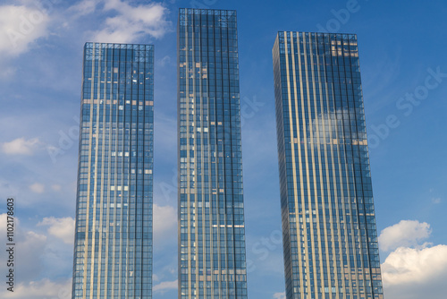 A clear view of three modern skyscrapers in Moscow, Russia, reaching towards a bright blue sky with fluffy white clouds.