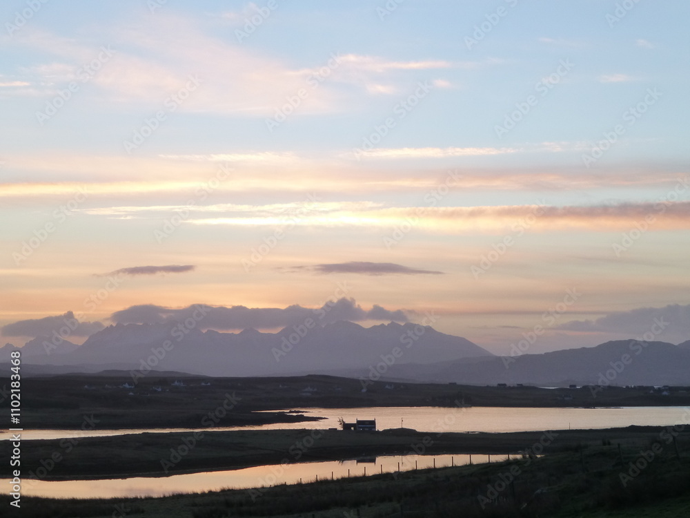 Sunset sky over the Cuillin mountains, Skye, Scotland, with Pool Roag and single silhouetted cottage in the foreground Sunset sky over the Cuillin mountains, Skye, Scotland, with Pool Roag and single silhouetted cottage in the foreground