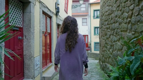 Young woman enjoys walking in narrow alley way in Porto city in Portugal. Female tourist looking around old medieval buildings and colorful facades and ancient walls. Sightseeing in Europe