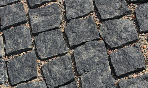 An angled view of evenly laid rows of dark granite paving stones
