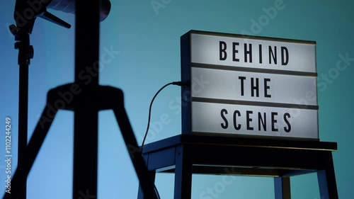 Behind the scene light box in front of vdo camera frame. Black text on white lightbox of word Behind the scenes. Prop for filmmaker movie or film studio. Footage for B roll video production making of.