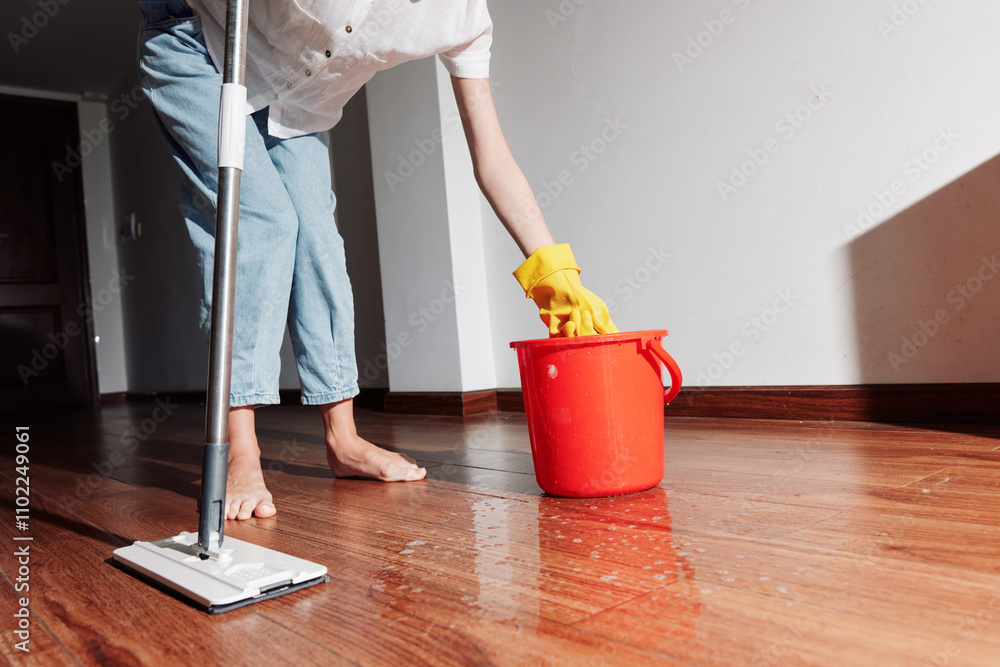 Woman cleaning hardwood floor with water bucket and mop in room corner Woman cleaning hardwood floor with water bucket and mop in room corner