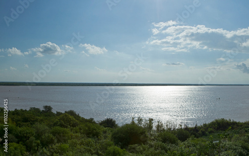 Aerial view of the green tropical jungle and river at sunrise. The bright sun reflection in the surface of the water.
