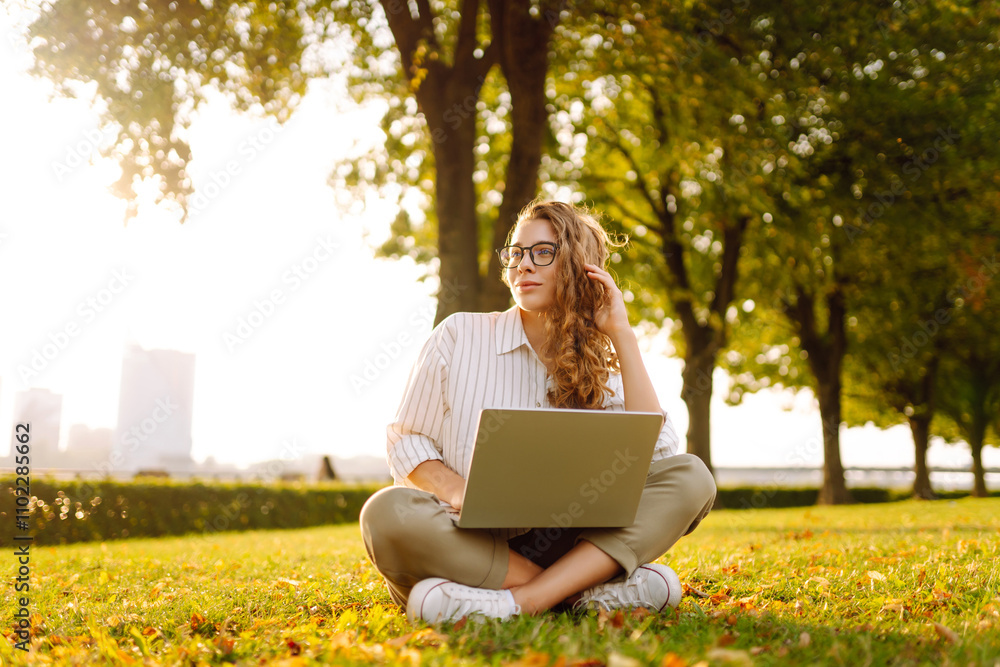 Happy woman sitting on a green clearing with a laptop. Freelancer, education online. Communication online. Happy woman sitting on a green clearing with a laptop. Freelancer, education online. Communication online.