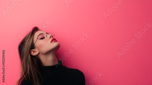 A young woman standing in front of a bright pink background. She is wearing a black turtleneck and glasses, with her head tilted back and her eyes closed.