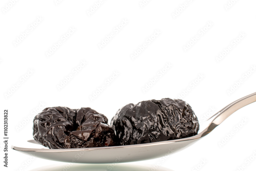 Sweet prunes with a metal spoon, macro, isolated on a white background.