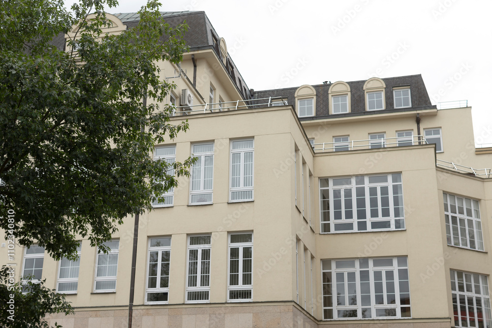 A large architectural building featuring numerous windows, complemented by a beautiful tree strategically located in front of it A large architectural building featuring numerous windows, complemented by a beautiful tree strategically located in front of it