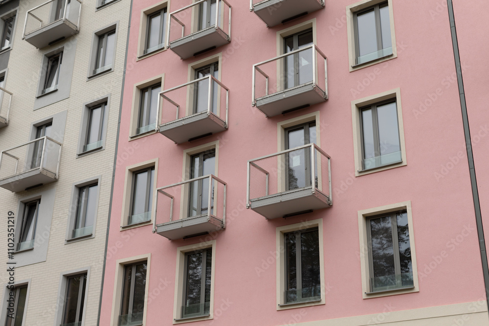 Fototapeta premium A pink and white apartment building stands tall, featuring multiple balconies and a variety of windows that adorn its facade