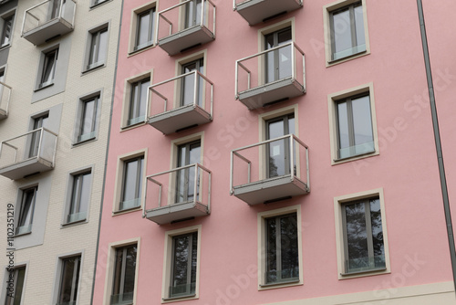 A pink and white apartment building stands tall, featuring multiple balconies and a variety of windows that adorn its facade