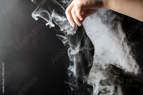 Photography human hand, recoiling disgust, holds black sock emanating pungent gray smoke