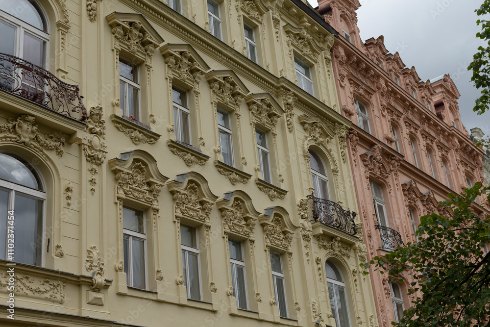 In a row, there are several buildings showcasing numerous windows and balconies, all observed on a cloudy day in the city In a row, there are several buildings showcasing numerous windows and balconies, all observed on a cloudy day in the city