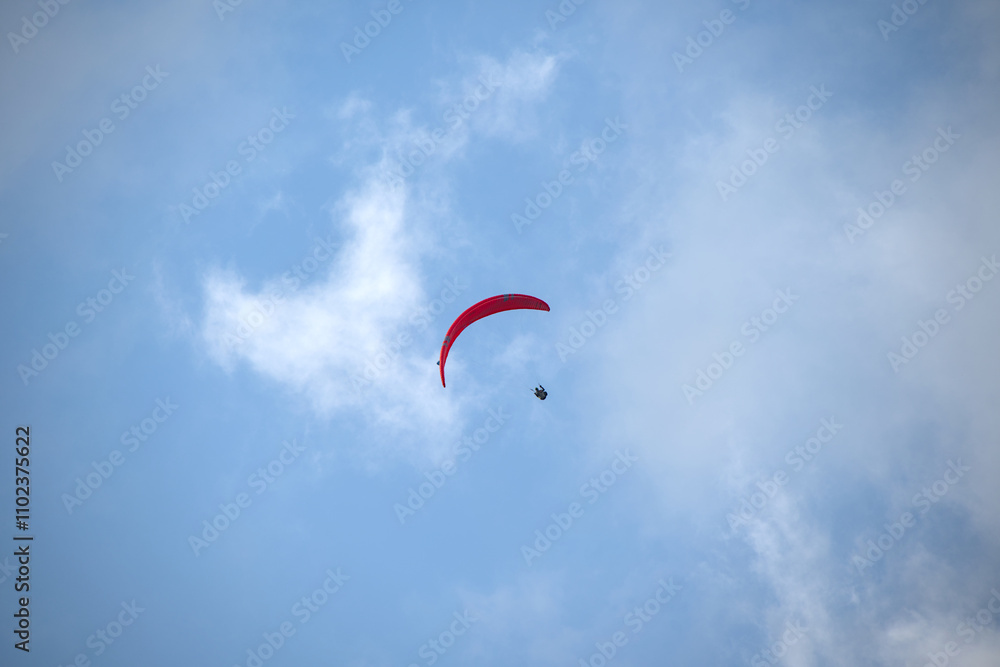 Paraglider with a vibrant red canopy gliding through the sky surrounded by soft white clouds. Paraglider with a vibrant red canopy gliding through the sky surrounded by soft white clouds.