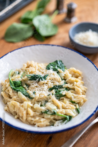 Orzo noodles in cream sauce with spinach on wooden table 