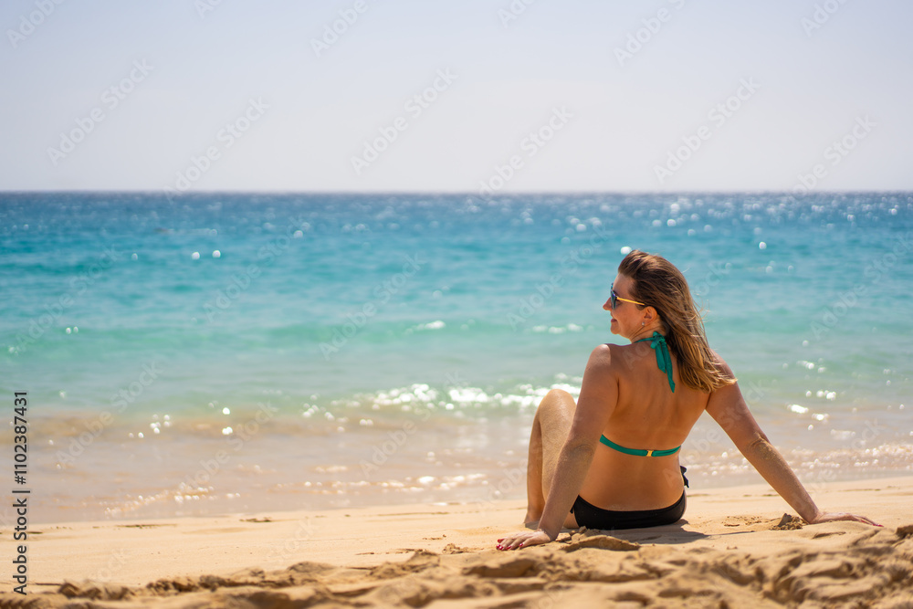 Tropical beach. Happy mature woman in bikini lying down on sandy beach by ocean. Positive vibes. Back view Tropical beach. Happy mature woman in bikini lying down on sandy beach by ocean. Positive vibes. Back view