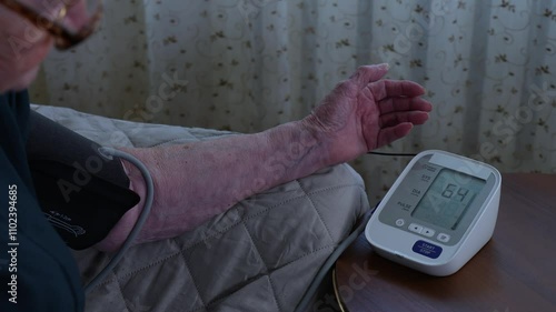 Elderly person's hand operating home blood pressure monitor. Accessible technology enabling self-care and self-monitoring of wellness metrics.