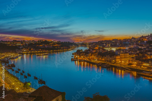 Blue sky is reflected on the river Douro between Porto and Gaia with golden colours of the sunset at dusk. The night lights illuminate the city streets and buildings.