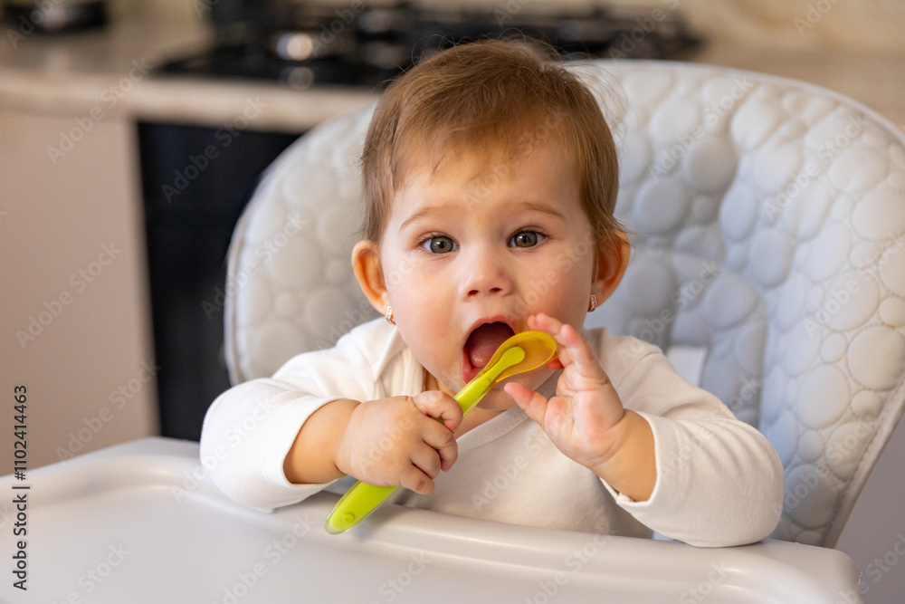 Small cute little toddler kid girl with a spoon sitting in baby chair and waiting for food. Self-feeding concept. First solid food. Children meal concept. High quality photo Small cute little toddler kid girl with a spoon sitting in baby chair and waiting for food. Self-feeding concept. First solid food. Children meal concept. High quality photo
