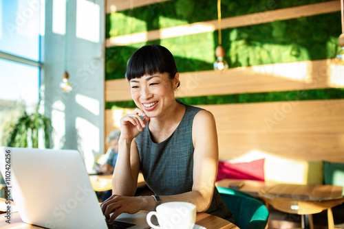Smiling young Asian businesswoman working with laptop in modern cafe