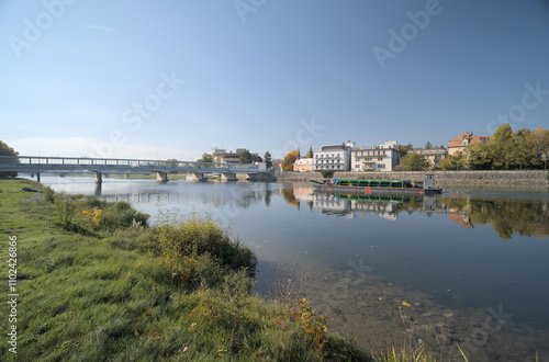 Riverside town with buildings and trees reflecting in calm water.