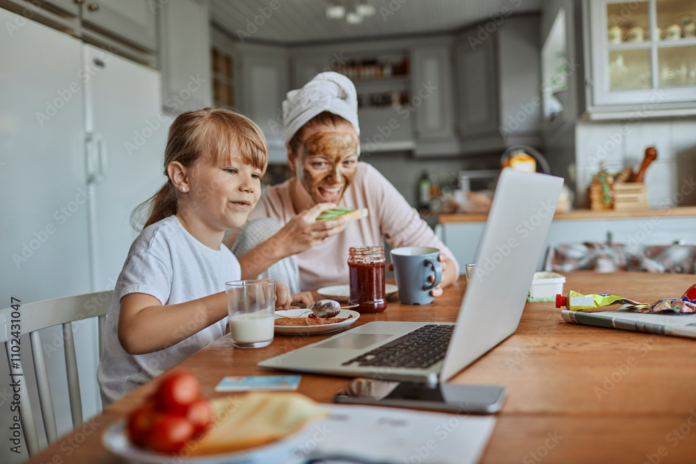 Mother and daughter having breakfast and watching laptop together in cozy kitchen Mother and daughter having breakfast and watching laptop together in cozy kitchen