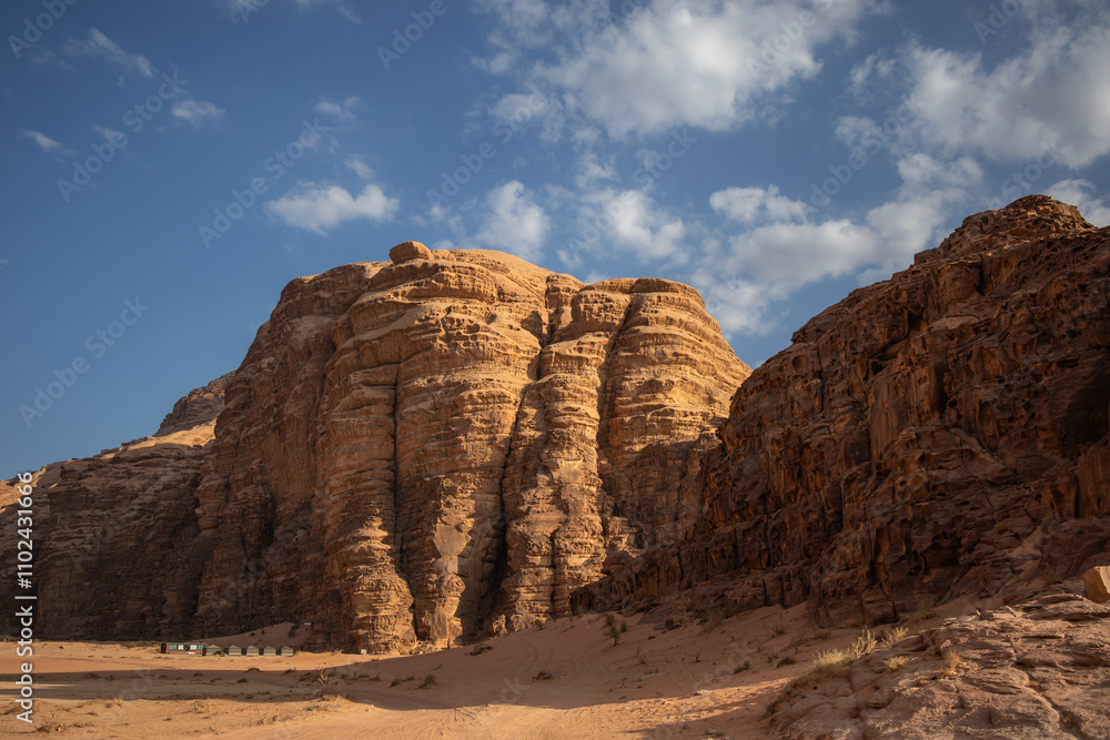 Fototapeta premium Sandstone Rock Formation in Sunny Desert in Southern Jordan. Wadi Rum Landscape with Rocky Mountain and Sandy Surface in the Afternoon.