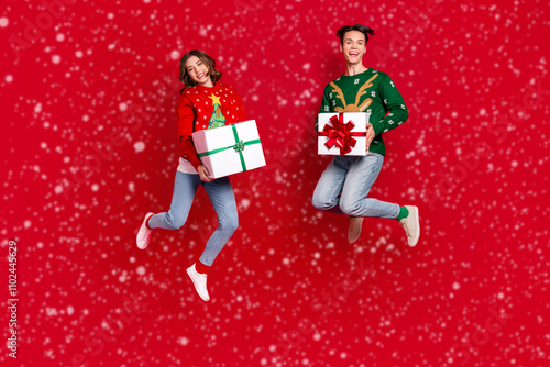 Full body photo of overjoyed energetic people jumping hands hold newyear festive giftbox isolated on red color background