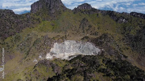 Aerial view  4K of caldera of ancient volcano covered with green forest, and village on its top with clouds flying above it. Sumbing Mountain, Indonesia