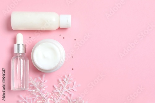 Winter skin care concept. Cosmetic products packaging design. Dropper bottle with serum, moisturizer cream jar and snowflake on color background. Flat lay, top view.