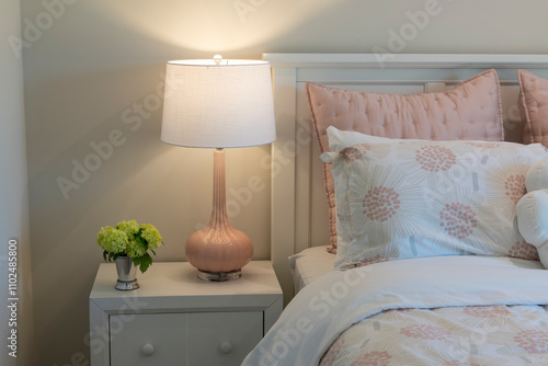 Delightful kids bedroom corner featuring pastel bedding, a pink bedside lamp, and a white nightstand with a floral touch, evoking warmth and charm.