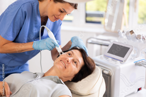 Fotografie Positive mature woman undergoing radiofrequency skin tightening procedure to improve facial skin tone and smooth out wrinkles